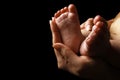 Beautiful baby baby feet on the handle of the parent hands on a black background Royalty Free Stock Photo