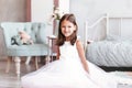 Beautiful baby girl sits on the floor in a light bedroom in a white dress. A look at the camera Royalty Free Stock Photo