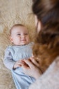 A beautiful baby lies on his back and looks happily at his mother, who holds him by the handles Royalty Free Stock Photo