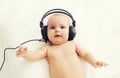 Beautiful baby listens to music in headphones lying on bed