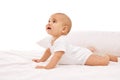 Beautiful baby, little girl in white comfortable clothes lying on belly on bed with pillow behind against white Royalty Free Stock Photo