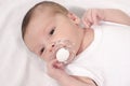 Beautiful baby lying down on white sheets with a pacifier in his mouth.
