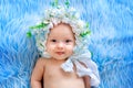 Beautiful baby 6 months in a hat made of flowers, lying on a blue background of fur, a small child in a flower wreath