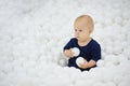 Beautiful baby sits in dry pool of white balls, looks away Royalty Free Stock Photo