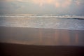 Beautiful background with sand beach reflecting pink morning clouds. Ocean shore with waves rolling on shore. Royalty Free Stock Photo