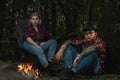 Beautiful Backpacker Woman And Man Having Rest Near Bonfire After Hiking In Forest. Contains chrominance noise Royalty Free Stock Photo