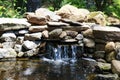 Beautiful backyard garden pond with natural river stones and clear waterfall Royalty Free Stock Photo