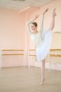 Beautiful ballerina in body and white tutu is training in a dance class. Young flexible dancer posing in pointe shoes.