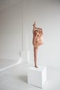 Beautiful ballet dancer posing in the Studio performing the deflection in the back and leaning on a big cube