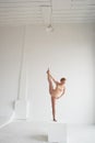 Beautiful ballet dancer posing in the Studio performing the deflection in the back and leaning on a big cube