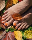 Beautiful bare woman feet close up. Orange pedicure on the autumn background. Yellow and red fallen leaves. Royalty Free Stock Photo