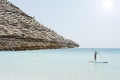 Beautiful beach resort with straw umbrellas on a blue sky and white clouds. On the background a man is surfing standing up with a Royalty Free Stock Photo