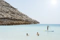 Beautiful beach resort with straw umbrellas on a blue sky and white clouds. On the background a man is surfing standing up with a Royalty Free Stock Photo