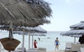 Beautiful beach resort with white straw umbrellas on a blue sky and white clouds. On the background some people having fun on the Royalty Free Stock Photo