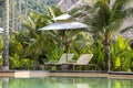 Tropical beach with swimming pool, coconuts palm trees, two deck chairs and umbrella near sea, Thailand Royalty Free Stock Photo