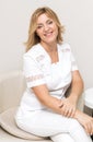 A beautiful beautician doctor in a white uniform smiles, looks into the camera and poses while sitting in a chair in her