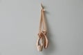 Beautiful beige ballet shoes with cute ribbons hanging on grey wall