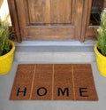 Beautiful Beige and black zute / coir Outdoor Door mat with `H O M E` text and vertical lines outside home with yellow flower pots Royalty Free Stock Photo