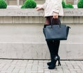 Beautiful big black handbag on the arm of the Incredible Long-legged brunette girl in a fashionable gray dress, posing