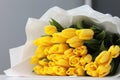 Beautiful big bouquet of yellow tulips in a white package on white table and gray wall background close up. Congratulation. Royalty Free Stock Photo