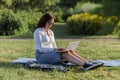 Beautiful big woman lying on the green grass in park with her laptop and working. Student girl looking at the computer screen Royalty Free Stock Photo