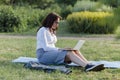 Beautiful big woman lying on the green grass in park with her laptop and working. Student girl looking at the computer screen Royalty Free Stock Photo