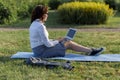 Beautiful big woman lying on the green grass in park with her laptop and working. Student girl looking at the computer screen Royalty Free Stock Photo