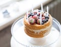 Beautiful biscuit cake with white cream decorated with strawberries blueberries and white candles standing on the stand at the win Royalty Free Stock Photo