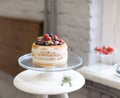 Beautiful biscuit cake with white cream decorated with strawberries and blueberries on a white pedestal stands at the window Royalty Free Stock Photo