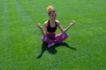 A beautiful black African-American woman in a sports black T-shirt and pink sneakers, relaxes sitting in a yoga pose and meditatin