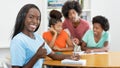 Beautiful black female student at desk showing thumb up with group of learning african american students Royalty Free Stock Photo