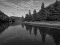 Beautiful black and white view of a creek with reflections of light clouds, mountains and trees on water Royalty Free Stock Photo