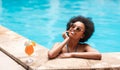 Beautiful black woman in blue bikini and sunlasses relaxing in swimming pool with cocktail drink, copy space Royalty Free Stock Photo