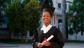 Beautiful black woman graduate posing with her diploma in front of the camera on the college garden she wearing