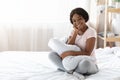 Beautiful black woman in pajamas sitting on bed, hugging pillow Royalty Free Stock Photo