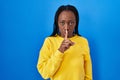 Beautiful black woman standing over blue background asking to be quiet with finger on lips Royalty Free Stock Photo