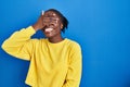 Beautiful black woman standing over blue background smiling and laughing with hand on face covering eyes for surprise Royalty Free Stock Photo