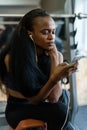 Beautiful black young woman with luxury long hair texting on her smartphone in the gym Royalty Free Stock Photo