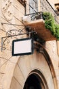 Beautiful blank sign in a forged metal frame hangs on a stone wall of a building against a background of balcony and Royalty Free Stock Photo