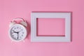 White wooden frame and white alarm clock on a nice pink background