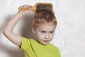 Beautiful blond baby boy brushing his golden hair with a wooden comb, pretty grimacing. Royalty Free Stock Photo
