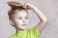 Beautiful blond baby boy brushing his golden hair with a wooden comb, pretty smiling. Royalty Free Stock Photo