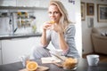 Beautiful blond caucasian woman posing in her kitchen, while drinking coffee or tea and eating a healthy breakfast meal full of ce Royalty Free Stock Photo