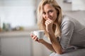 Beautiful blond caucasian woman posing in her kitchen, while drinking coffee or tea and eating a healthy breakfast meal full of ce Royalty Free Stock Photo