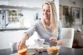 Beautiful blond caucasian woman posing in her kitchen, while drinking coffee or tea and eating a healthy breakfast meal full of ce Royalty Free Stock Photo