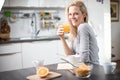 Beautiful blond caucasian woman posing in her kitchen, while drinking coffee or tea and eating a healthy breakfast meal full of ce Royalty Free Stock Photo