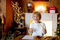 Beautiful blond child, young school boy, writing letter to Santa Claus in a decorated home with knitted toys