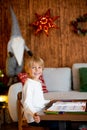 Beautiful blond child, young school boy, writing letter to Santa Claus in a decorated home with knitted toys