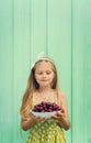 Beautiful blond girl on a background of turquoise wall holding plate with cherry. Royalty Free Stock Photo