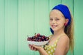 Beautiful blond girl on a background of turquoise wall holding plate with cherry. Royalty Free Stock Photo